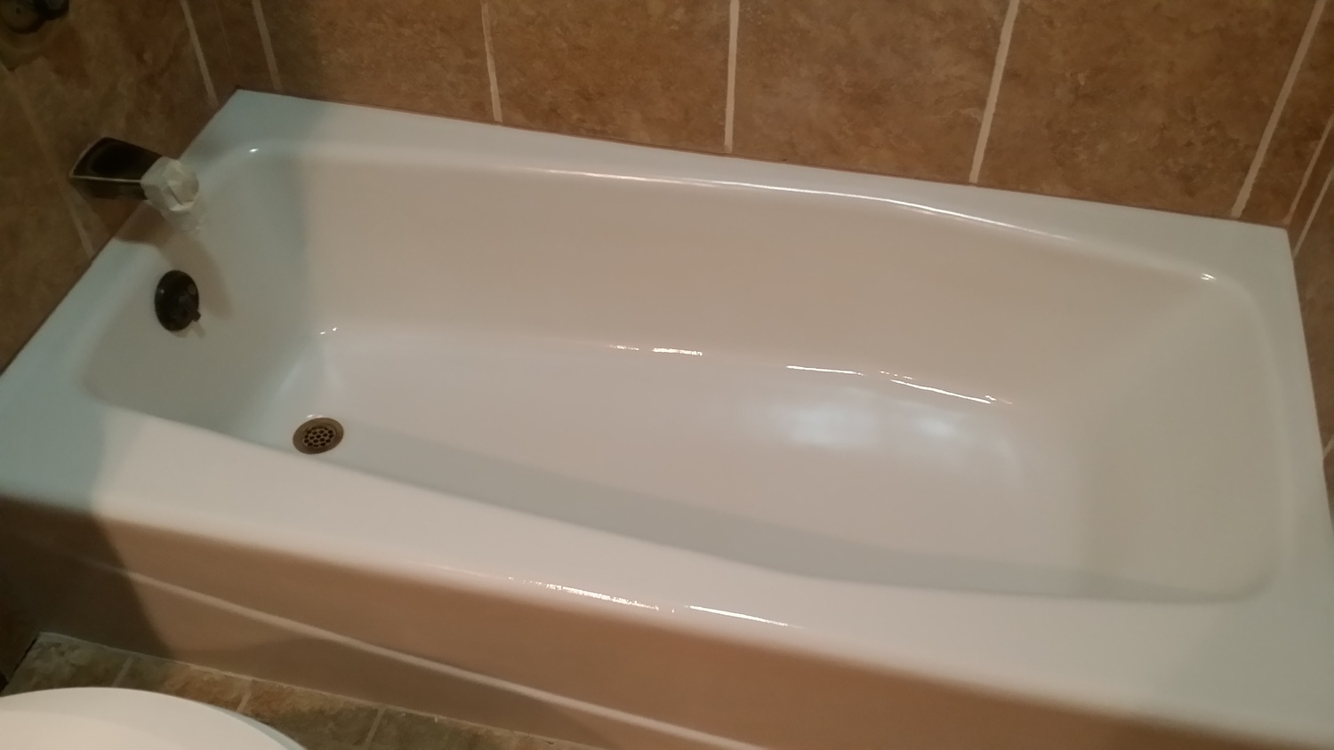 A Resurfaced or reglazed bathtub with a pure white finish. The tub is a baked porcelain over cast iron. Oil rubbed bronze finished drain and overflow